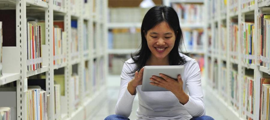 A woman sitting in a library aisle using a digital tablet