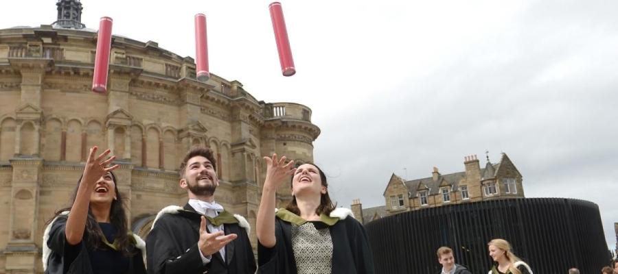 Graduates throwing red cylinders into the air outside McEwan Hall