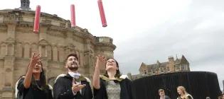 Graduates throwing red cylinders into the air outside McEwan Hall